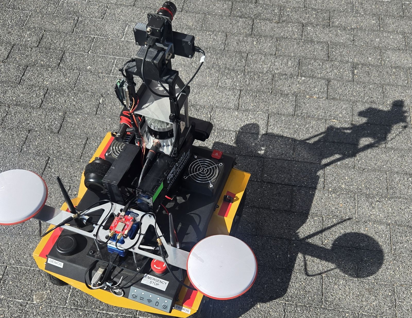 The Jackal and its sensor payload: the Ouster LiDAR that feeds the elevation map and the BEV segmentation network, a forward camera, GPS antennas, and the E-stop that makes outdoor testing survivable.